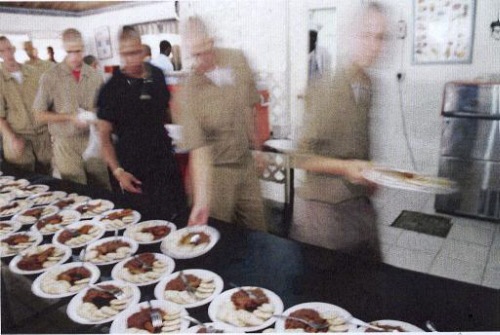 People beside a table of prepared plates. The image alone does not establish general meal conditions.